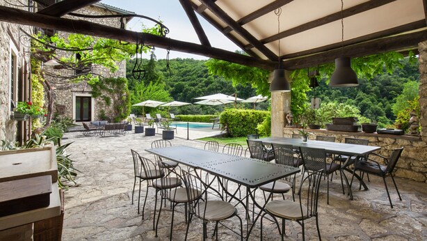 An outdoor patio with stone flooring, metal tables and chairs, umbrellas, and potted plants. - Il Giardino di Sibilla With Pool (Castelgomberto)