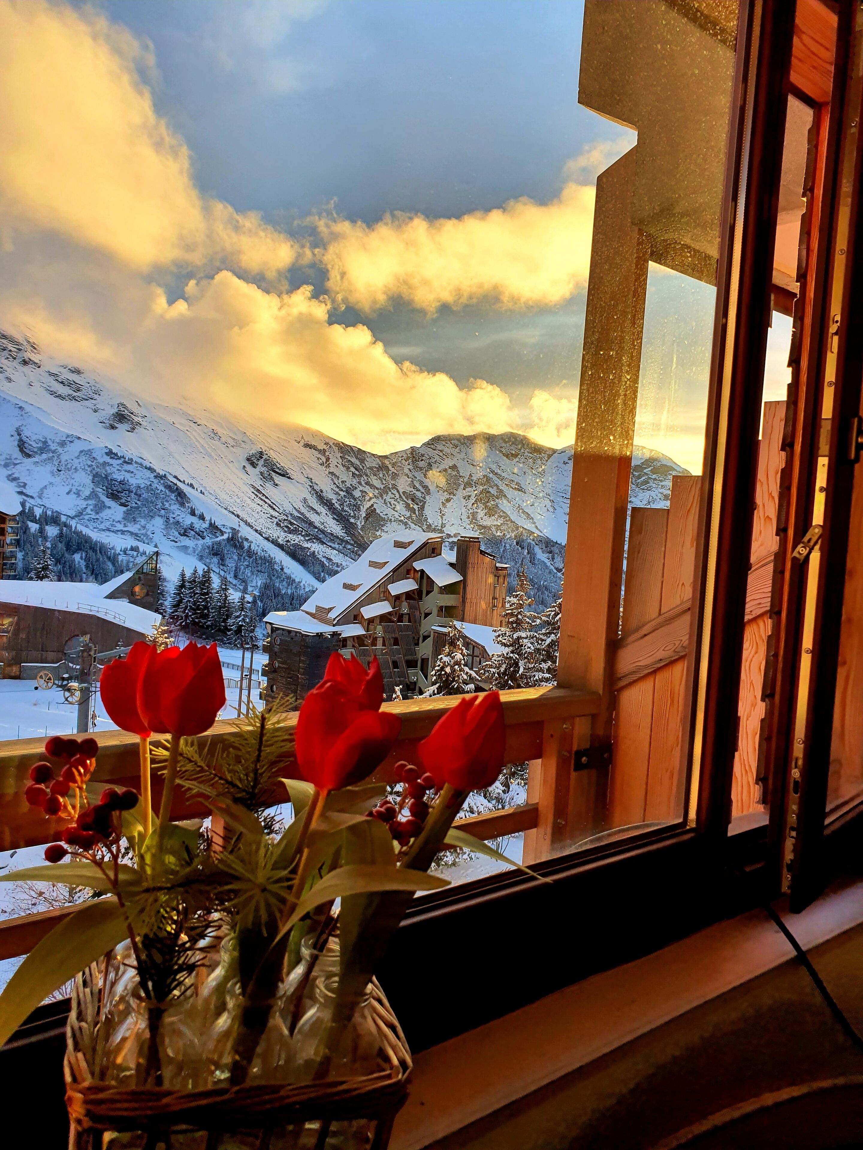 A view of snow-covered mountains and a wooden building through a window.