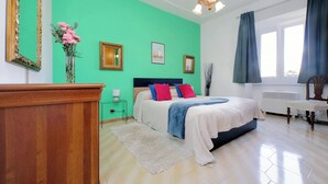 A bedroom with a bed, a dresser, a nightstand, a vase with flowers, and a window with curtains. - Red House Rome - Trastevere (Roma)