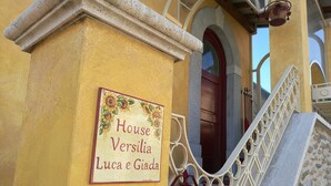Ein Gebäudeeingang mit einem Schild, das "House Versilia Luca e Giada" zeigt, und einer Treppe mit dekorativen Geländern.
