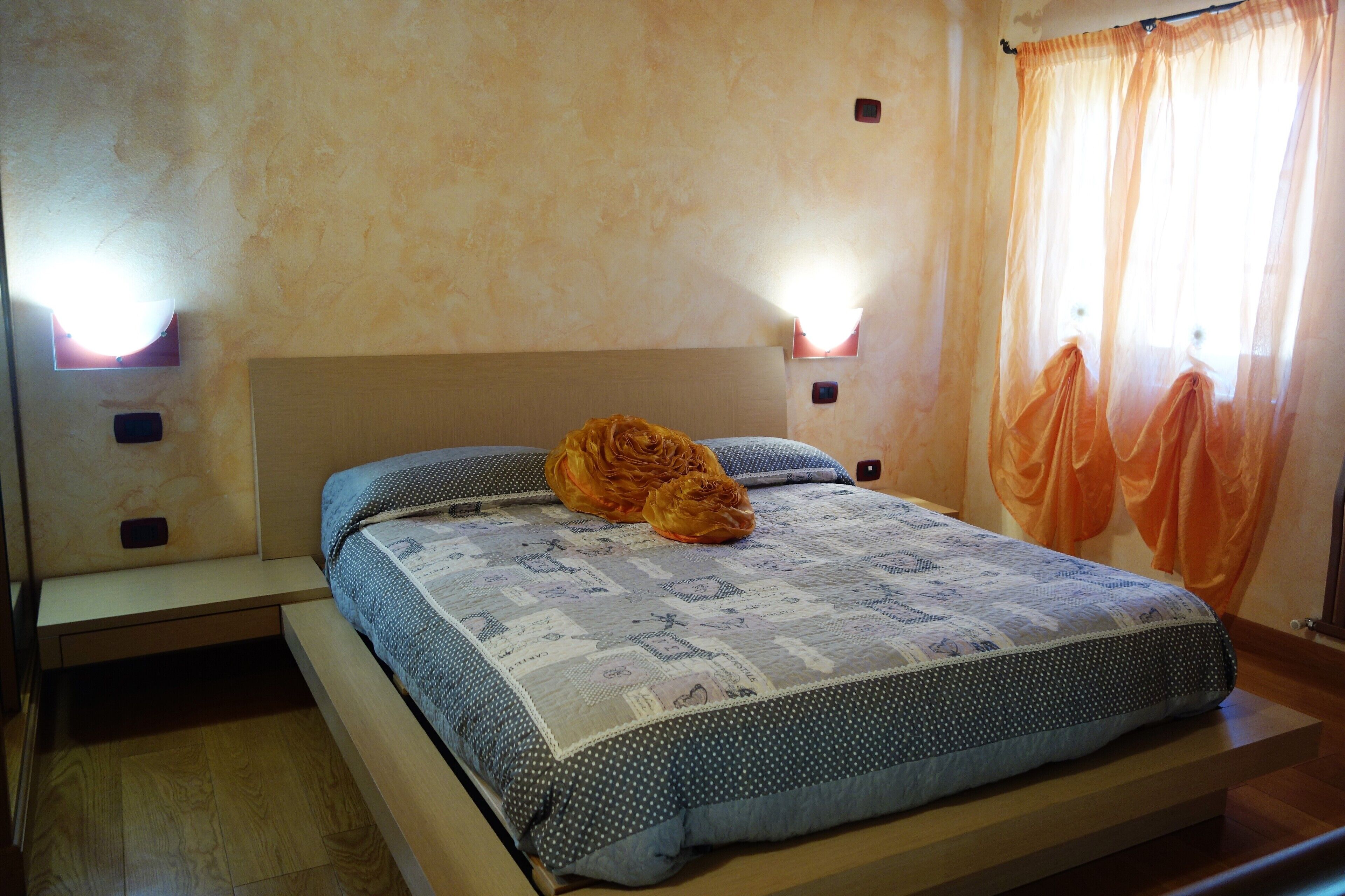 Quarto com uma cama, mesa de cabeceira e duas luminárias na parede.