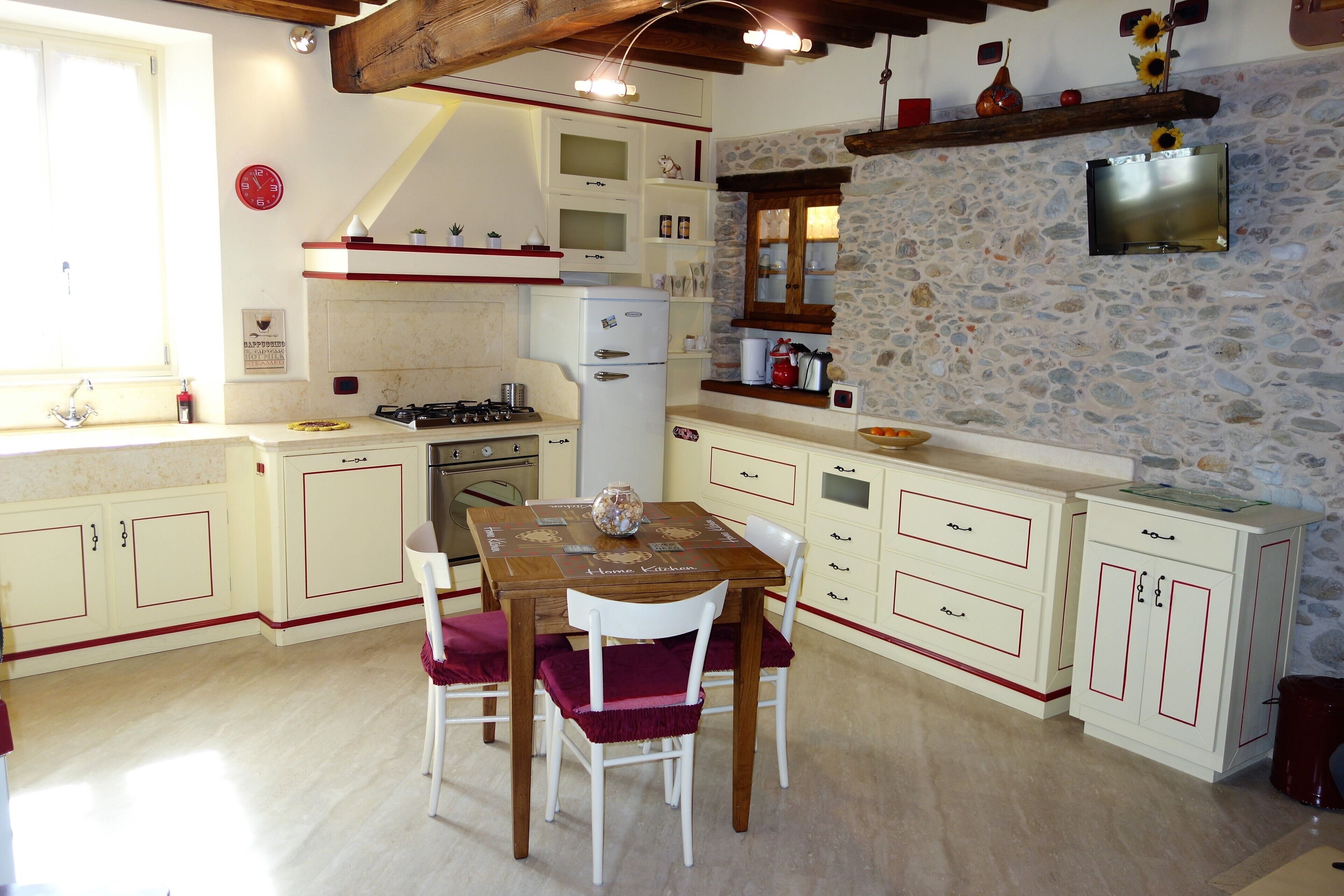 Una cucina con tavolo, sedie, frigorifero e una parete in pietra.