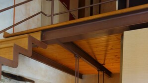 Eine Treppe mit hölzernem Geländer und Metallspindeln, die zu einer tiefer gelegenen Ebene führt.