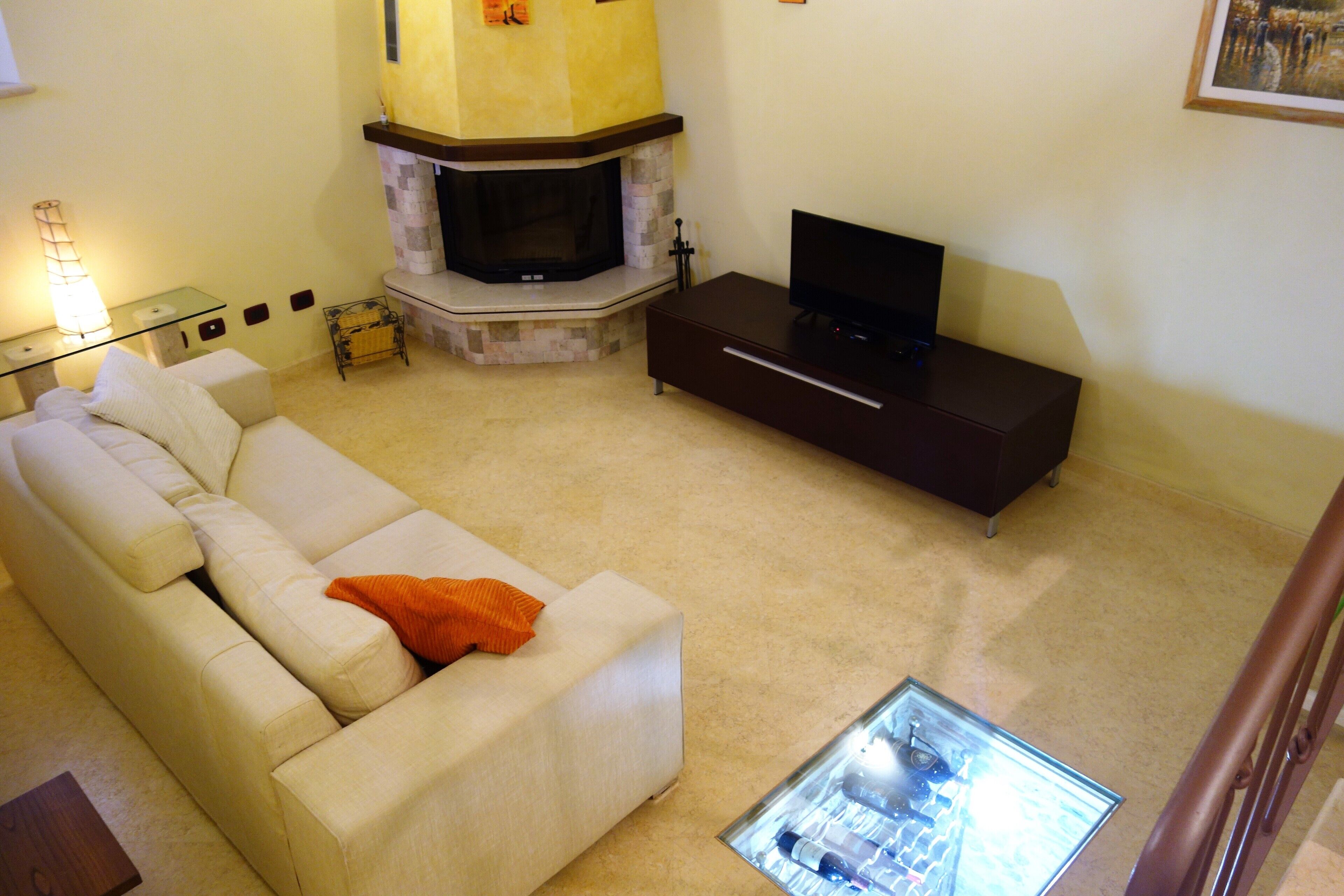 A living room with a beige sofa, a glass coffee table, a fireplace, and a flat-screen TV on a dark wooden stand.