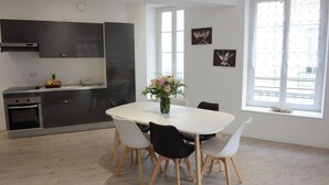 A modern kitchen with dark cabinets, a white dining table with four chairs, and a vase of flowers. - L'Échappée belle - Dieppe (Dieppe)