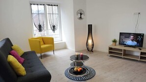 A modern living room with a black sofa, yellow armchair, and a TV on a wooden stand. - L'Échappée belle - Dieppe (Dieppe)