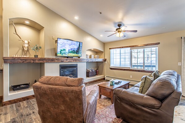 A living room with a fireplace, a television, and a ceiling fan. - Modern Mt Retreat |1 Mile from Steamboat Resort! (Steamboat Springs)