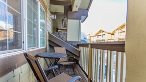Un balcon avec des fauteuils en osier et une petite table, des balustrades en bois et une vue sur les immeubles voisins.