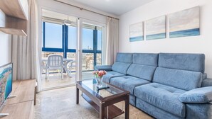 Ett vardagsrum med en blå soffa, ett soffbord i glas och utsikt över staden genom stora fönster.