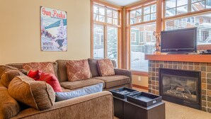 A cozy living room with a sectional sofa, a fireplace, and large windows. - Multi level 2 bedroom condo, easy access to ski trails (Sun Peaks)
