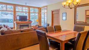A living room with a fireplace, a television, and a dining area with a table and chairs. - Multi level 2 bedroom condo, easy access to ski trails (Sun Peaks)