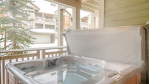 A hot tub on a wooden deck with a view of a building in the background. - Multi level 2 bedroom condo, easy access to ski trails (Sun Peaks)