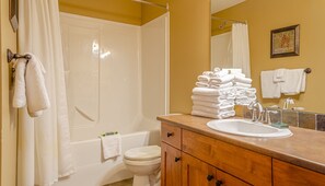 Une salle de bain avec une baignoire, des toilettes et un lavabo. Des serviettes sont pliées sur le lavabo et il y a un rideau de douche.
