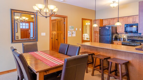 Un coin repas avec une table et des chaises en bois, une cuisine équipée d’appareils électroménagers modernes et un lustre.