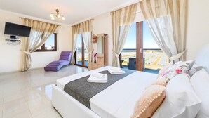 A hotel room with a large bed, a flat-screen TV, a sofa, and a view of the landscape. - Hann's Villa - Charming Kapparis Getaway (Protaras)