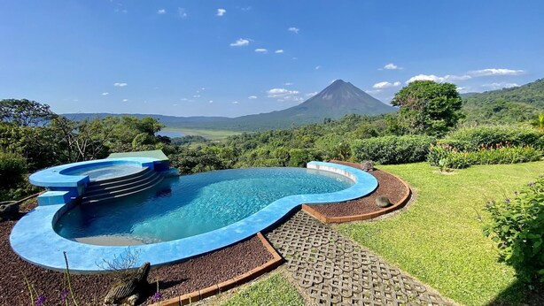 A swimming pool with a curved design, surrounded by a well-maintained lawn and a brick pathway.