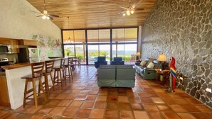 A spacious living area with a stone wall, a dining area with wooden chairs, a sofa, and a view of the outdoors.