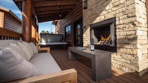 A wooden deck with a stone fireplace, a sofa, and a table with glasses and a bottle. - Blissful Mountain Getaway – Steps to Lake Estes, Indoor/Outdoor Fireplace (Estes Park)
