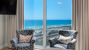 Ein Zimmer mit zwei gemusterten Sesseln, die auf ein großes Fenster mit Blick auf einen Strand zeigen.