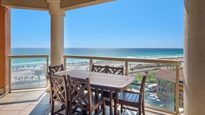Ein Balkon mit Holztisch und -stühlen mit Blick auf Strand und Meer.