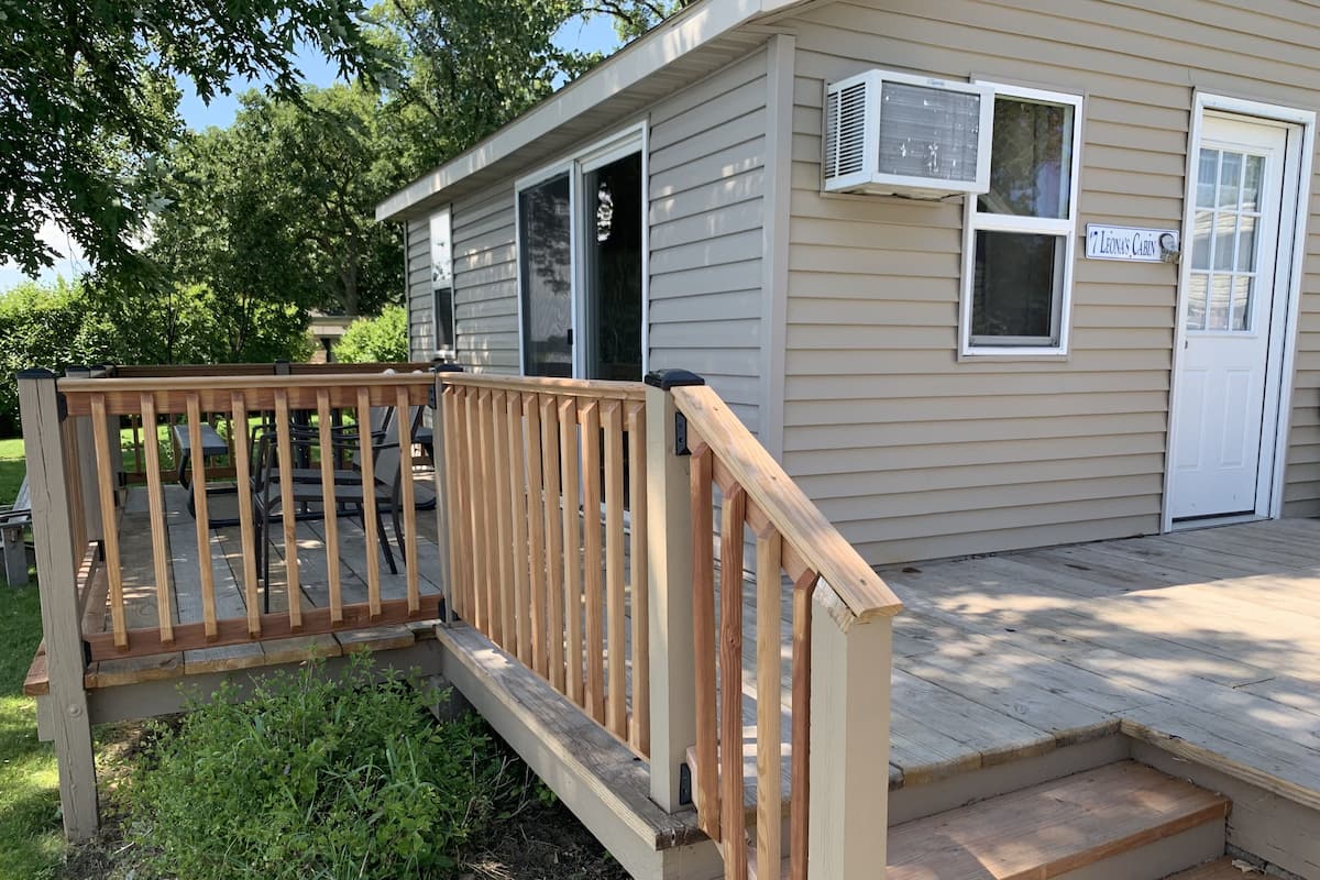 A small cabin with a wooden deck, a covered patio, and a door labeled "Leona's Cabin."