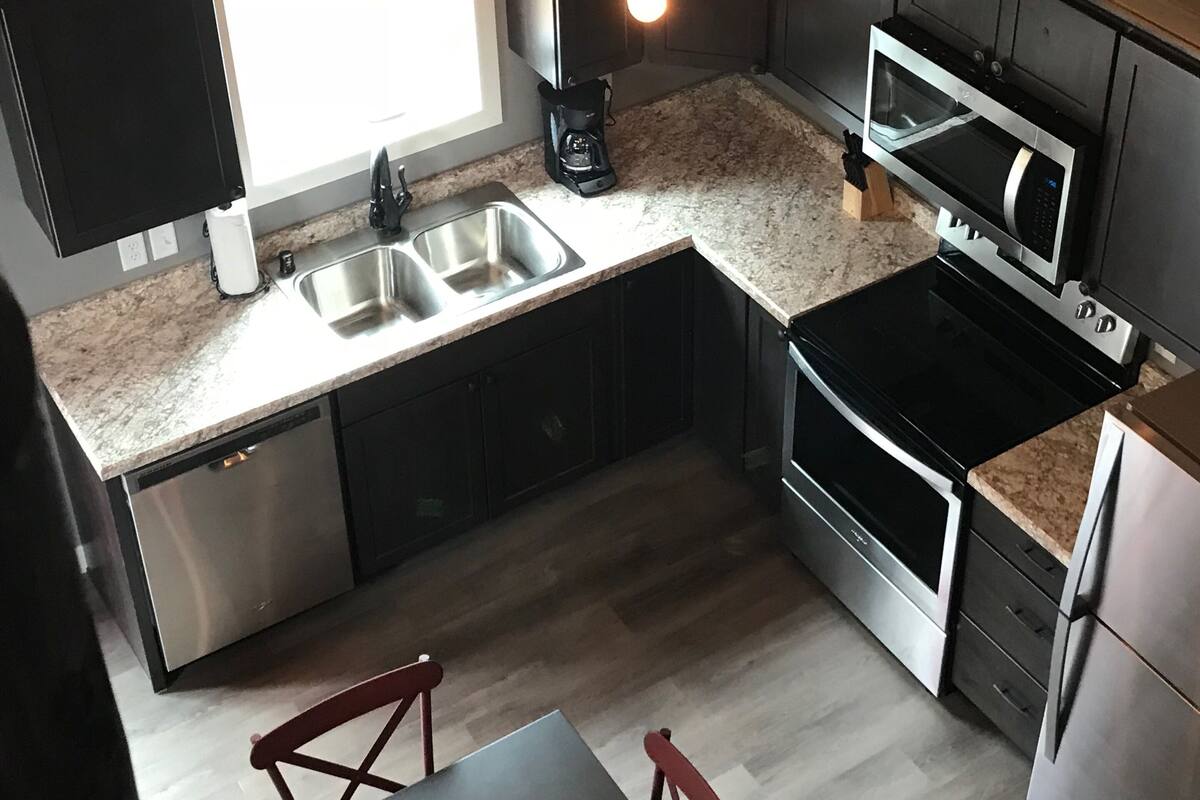 A modern kitchen with a built-in dishwasher, stainless steel appliances, a granite countertop, and a dining area with a table and chairs.