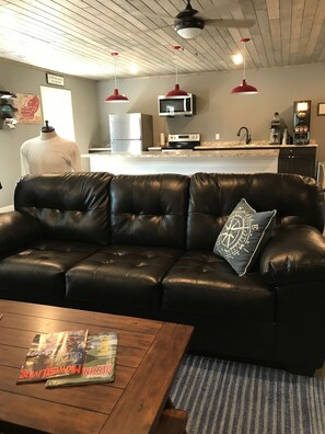 A living room with a black leather sofa, a wooden coffee table, and a striped rug. - Hollys Resort (Battle Lake)