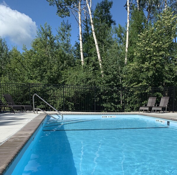 A clear blue swimming pool with a metal ladder, surrounded by a wooden deck and black lounge chairs. - Hollys Resort (Battle Lake)