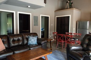 A living room with a leather sofa, wooden coffee table, and red chairs. There is a dining table with chairs and a refrigerator in the background. - Hollys Resort (Battle Lake)