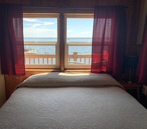 A bed with a view of the sea through a window with curtains. - Hollys Resort (Battle Lake)