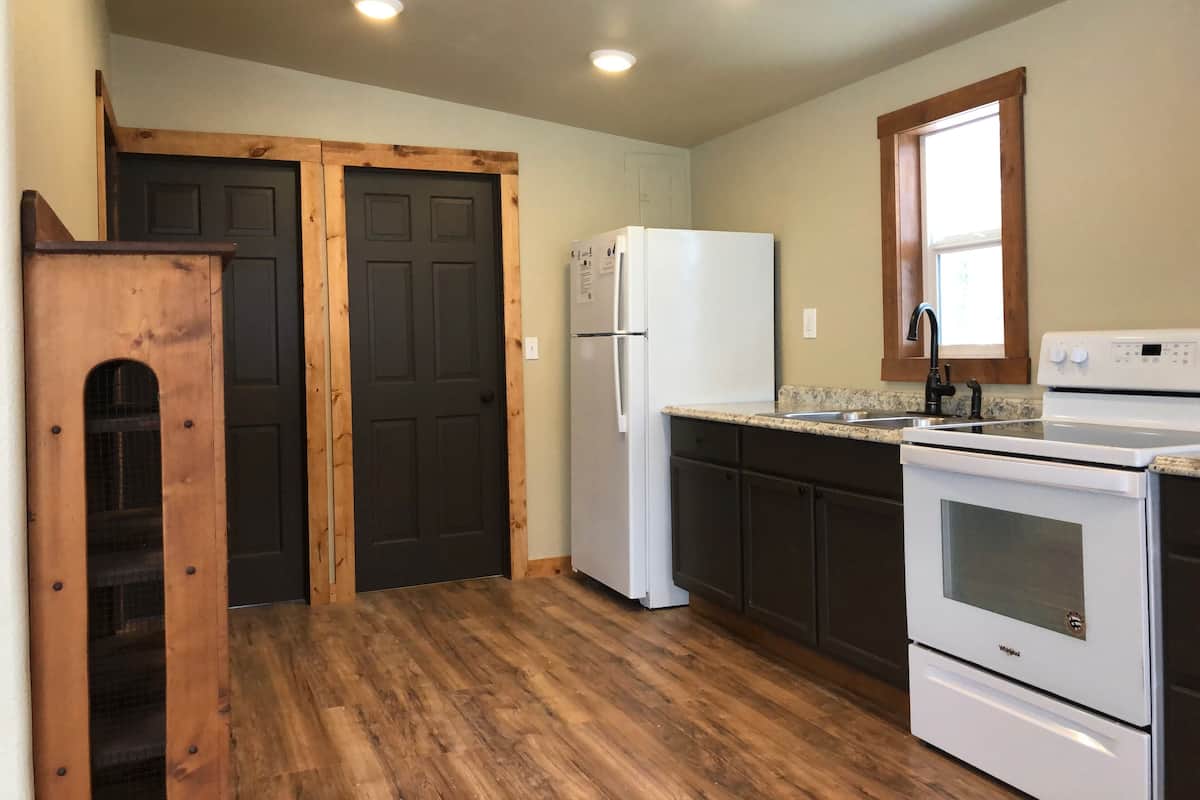 A kitchen with wooden floors, a white refrigerator, a stove, and a window with a wooden frame.