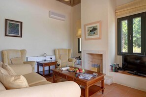 Un salon comprenant un canapé, des fauteuils, une table basse, une cheminée, un téléviseur et des étagères.