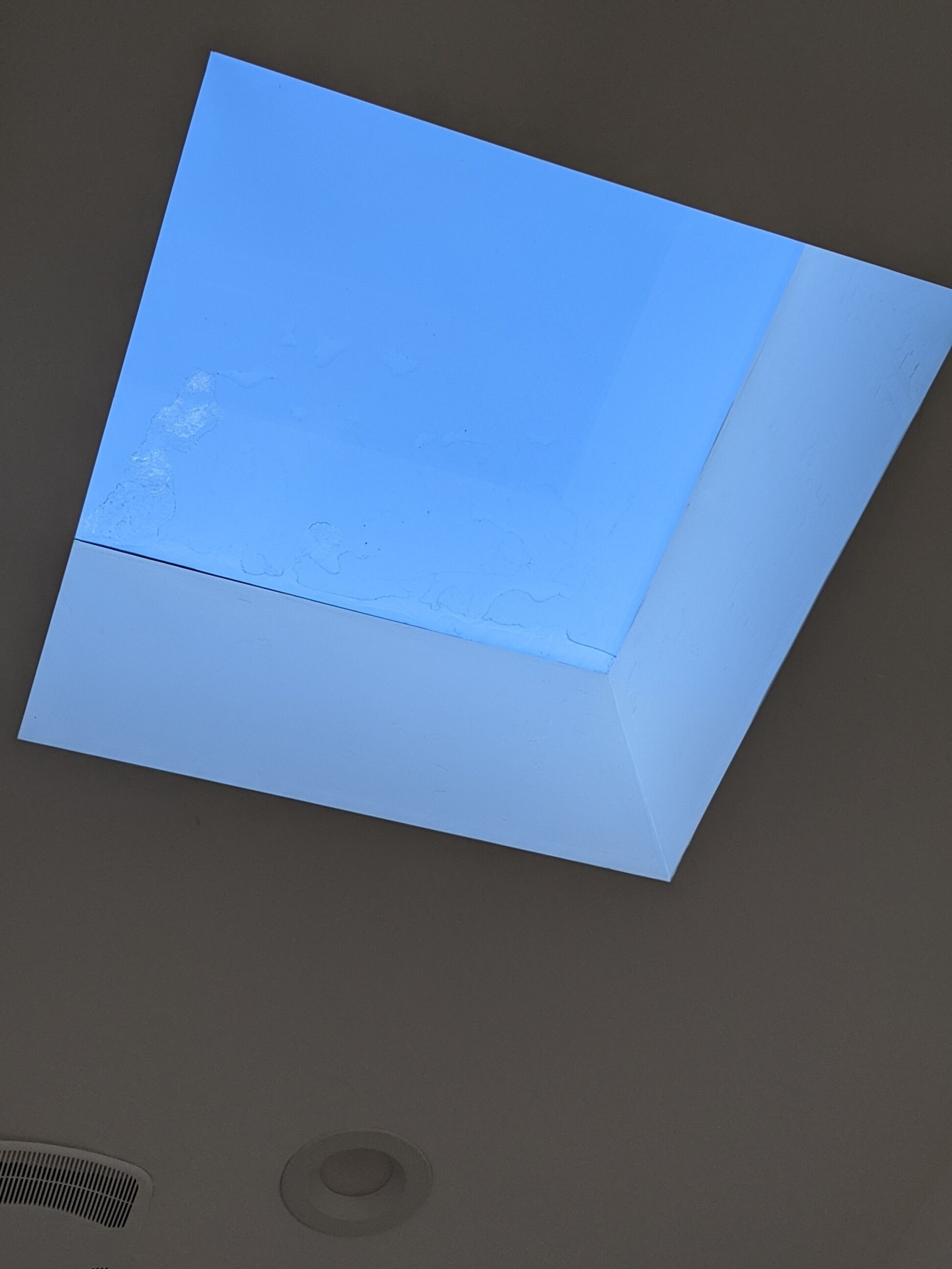 Techo con una luminaria empotrada y una rejilla de ventilación.