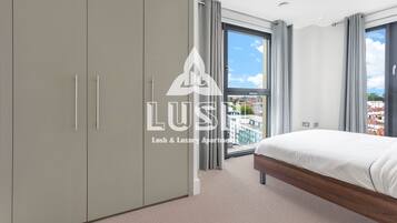 A modern bedroom with a large bed, grey wardrobe, and a balcony with a city view.