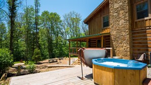 Eine Holzterrasse mit Whirlpool, ein Steinhaus und ein bewaldeter Bereich.