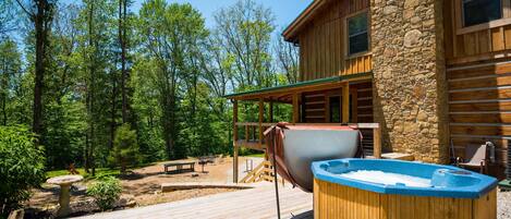 A wooden deck with a hot tub, a stone building, and a forested area.
