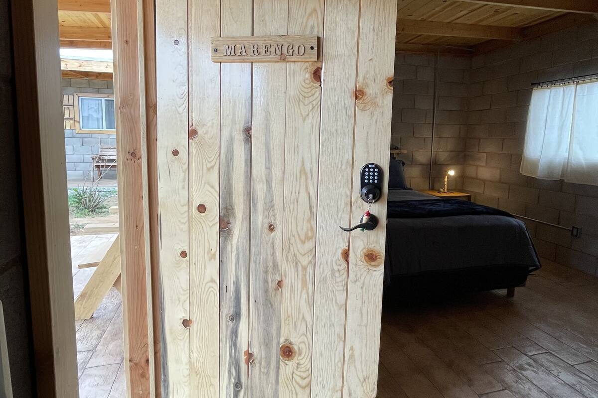 A wooden door with a nameplate reading "MARENGO" in a room with a bed, a bedside table, and a window.