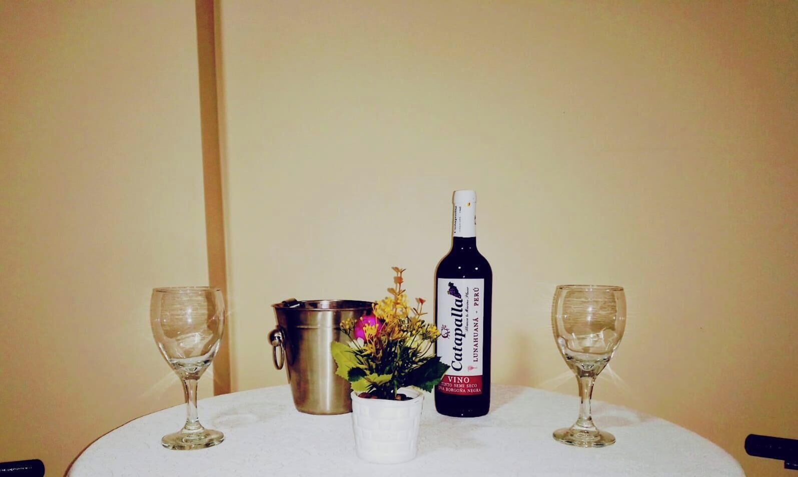 A table with a bottle of Catapalla wine, a flower arrangement, and two empty wine glasses.