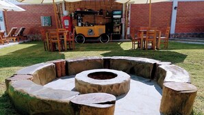 Een ronde vuurkuip van steen met zitplaatsen eromheen, een klein geel voertuig, en buitentafels en stoelen.
