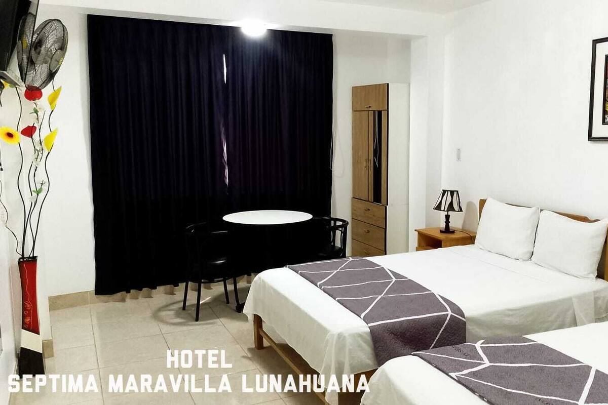 Ein Hotelzimmer mit zwei Betten, einem Schreibtisch, einem Stuhl, einem Tisch und einem Bild an der Wand.