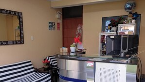 Een ontvangsthal met een gestreepte bank, een receptiebalie, een spiegel en een muur met een 'SALIDA' bord.