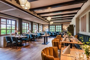 En rummelig restaurant med flere spiseområder, store vinduer og moderne lysarmaturer.