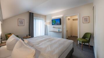 A hotel room with a large bed, a television mounted on the wall, a chair, and a small table with a lamp.