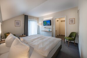 A hotel room with a large bed, a television mounted on the wall, a chair, and a small table with a lamp. - Standard Double Room - Landhotel Zur Eiche (Buxtehude)