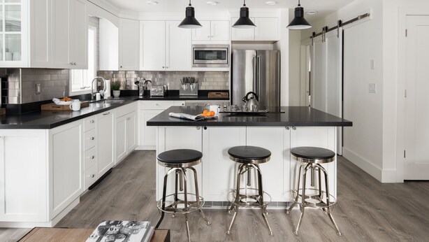 Una cocina moderna con armarios blancos, encimera negra, electrodomésticos de acero inoxidable y tres taburetes de bar.