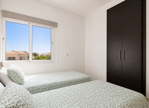 Ein Schlafzimmer mit zwei Betten, einem Fenster und einem dunklen Kleiderschrank.