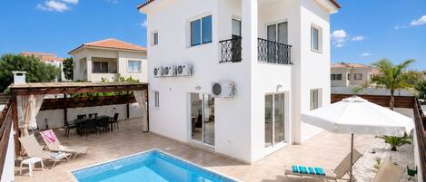 A two-story building with a swimming pool, outdoor seating, and a covered patio area.