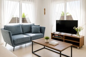 Ein modernes Wohnzimmer mit einem grauen Sofa, einem Couchtisch, einem Fernseher auf einem Holzständer und einem Bücherregal.