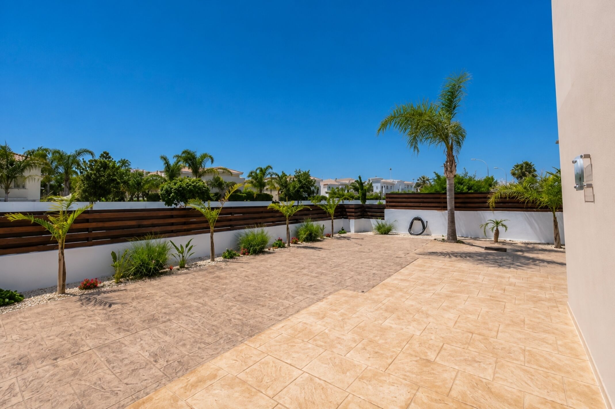 A courtyard with a tiled floor, a wooden fence, and a palm tree.