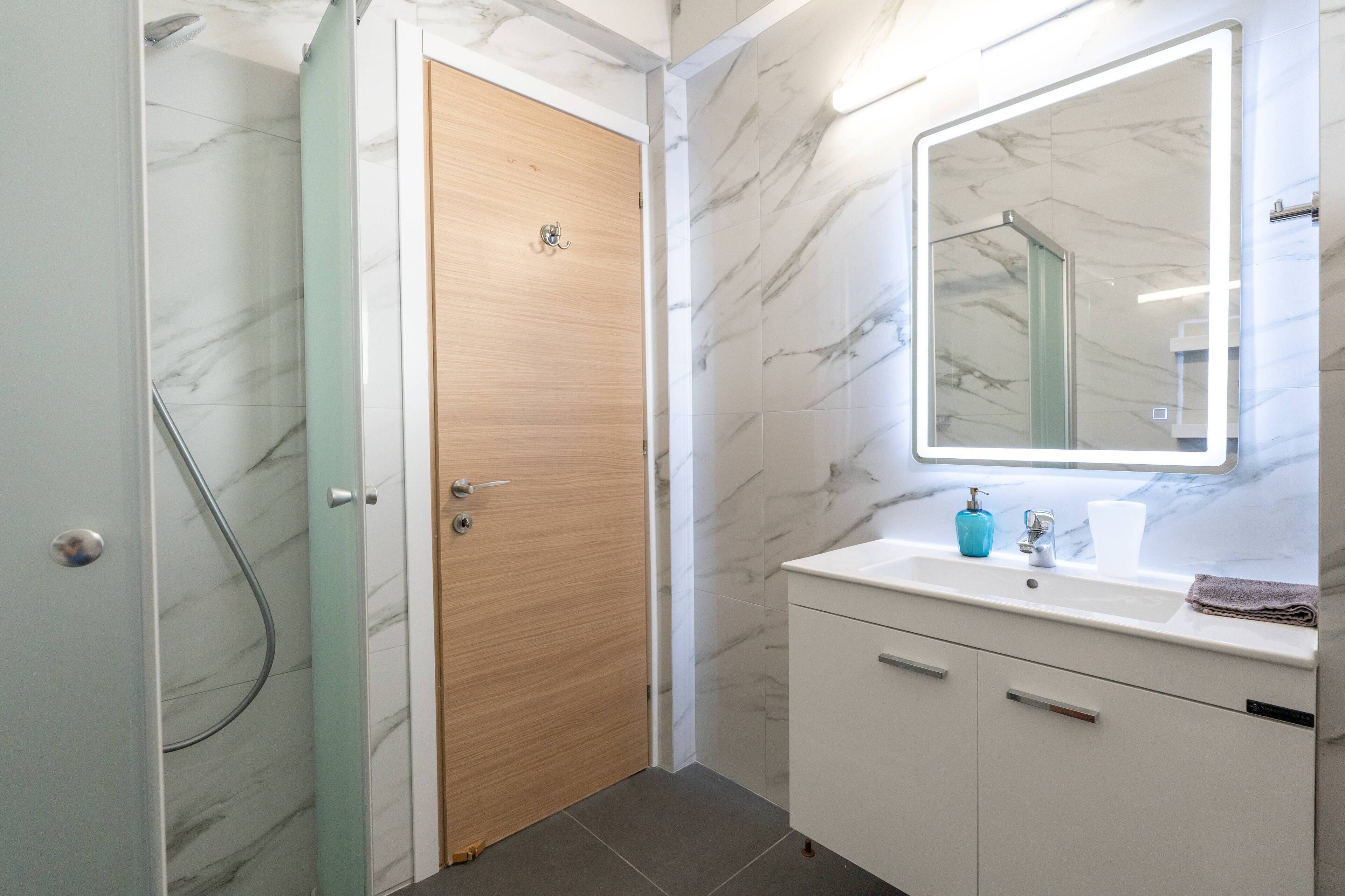 A bathroom with a wooden door, a sink with a mirror, and a shower area.